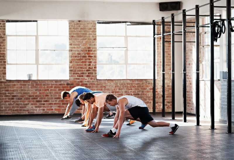 Grupo de atletas realizando ejercicios de calentamiento, estiramientos de piernas y movilidad en el gimnasio antes del entrenamiento de fuerza de Bilbo Team.