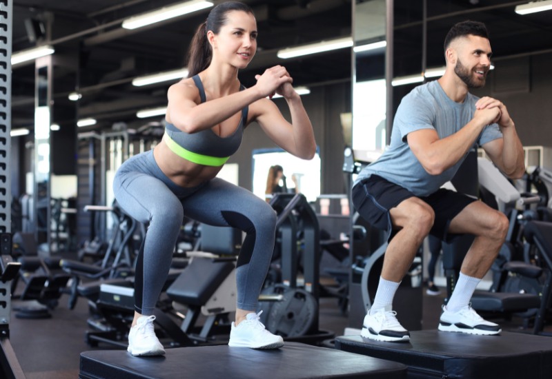 Hombre y mujer realizando sentadillas en el gimnasio dentro de una rutina de entrenamiento de piernas para fuerza e hipertrofia de Bilbo Team.