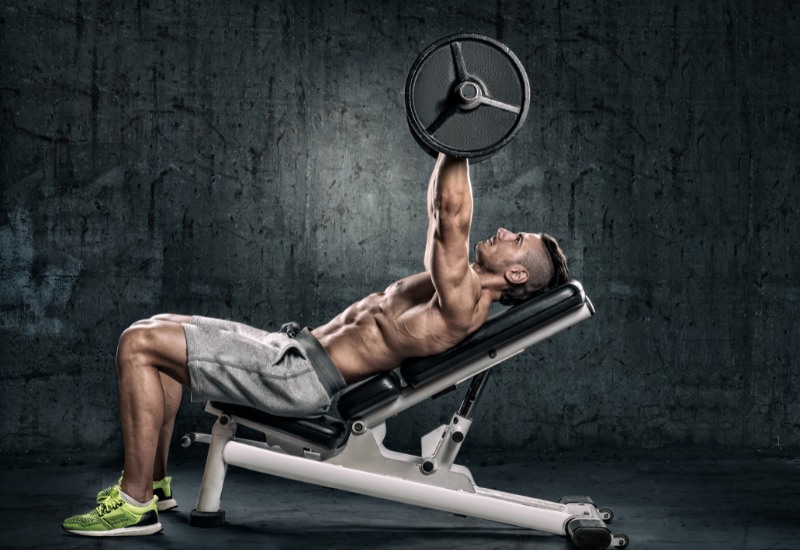 Deportista ejecutando un press de banca inclinado en un banco regulable a 30 grados para enfatizar el trabajo de la porción clavicular del pectoral.